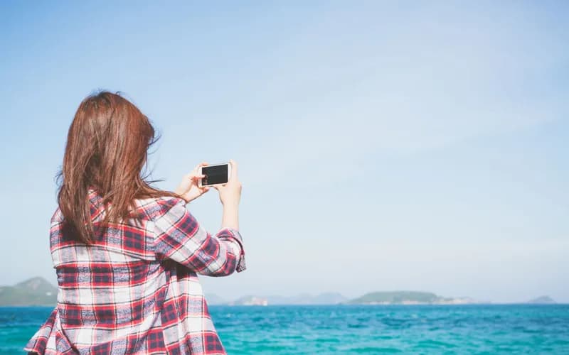 a traveler holding a smartphone showing a mobile signal on a Thai beach