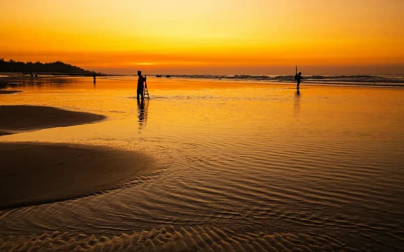 Une plage tropicale isolée au crépuscule, vue grand angle, collines boisées sombres s'élevant derrière un rivage de sable pâle, mer calme en reflet