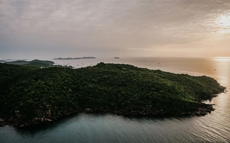 Vue aérienne d'un petit archipel tropical à l'heure dorée, forêt dense couvrant des collines escarpées, sable pâle