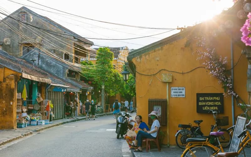Une rue calme d'une ville côtière au crépuscule, bâtiments coloniaux bas aux façades patinées, quelques motos garées le long de la route