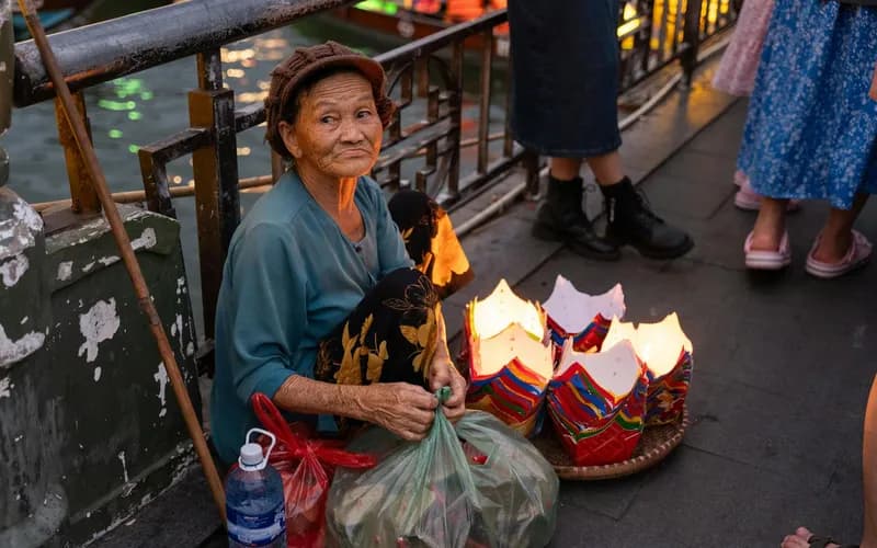 Une femme disposant de petites coupes en céramique de bánh bèo sur une table en bois basse au bord de la rivière des Parfums à l'aube, lumière matinale argentée et douce