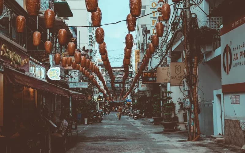 Une ruelle étroite aux lanternes allumées dans le vieux quartier de Hue au crépuscule, quelques silhouettes au loin, lumière dorée et chaude se déversant des façades