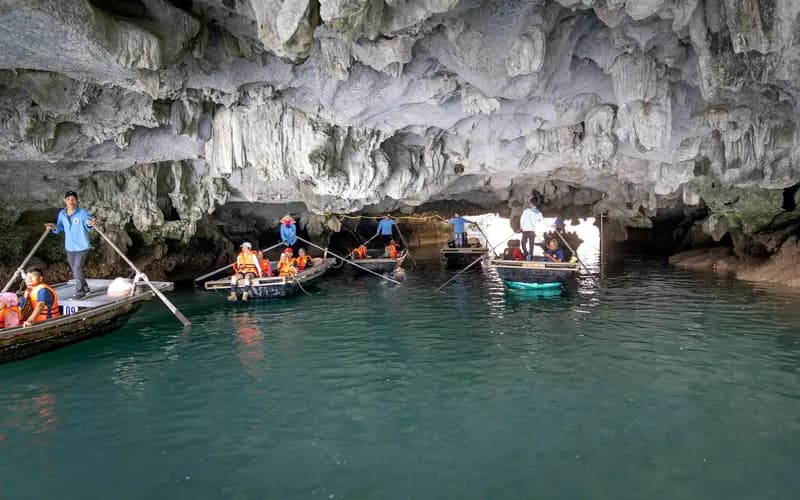 Interior of a limestone cave grotto viewed from a wooden sampan, low ceiling with stalactites, soft green water reflecting di