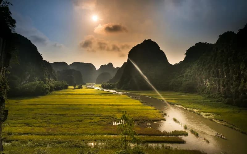 A narrow concrete cycling path through flat rice paddies at golden hour, limestone karst towers in the background, a lone cyc