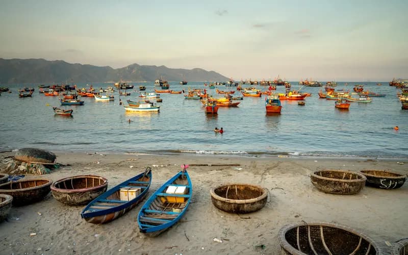Un village de pêcheurs tranquille sur une baie sablonneuse en courbe au crépuscule, petits bateaux en bois amarrés dans des eaux peu profondes, lumière orange chaude