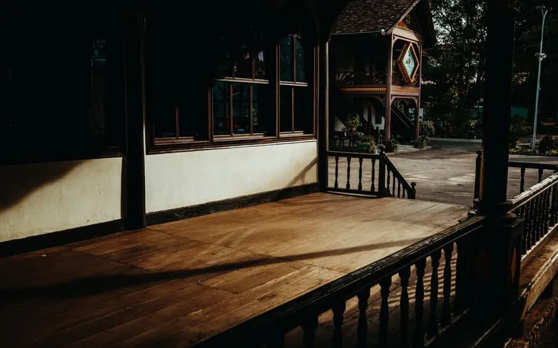Interior of a traditional Thai stilt house homestay at golden hour, warm lamplight, wooden floors and low furniture, a view t
