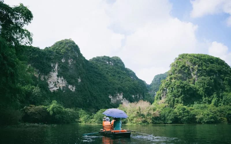 A wooden rowing boat on a narrow river winding through tall limestone cliffs and green rice paddies, overcast morning light,