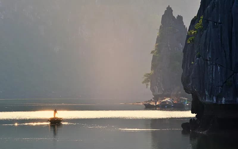 Wide view of a small Vietnamese fishing bay at dawn, round coracle boats on calm grey-green water, wooden fishing vessels moo