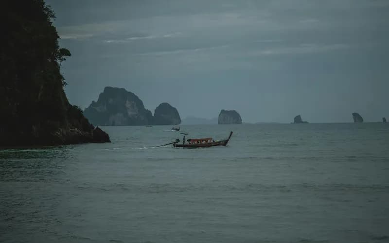 Un bateau en bois sur une eau calme et lisse dans une baie du sud du Vietnam en début de matinée, lumière douce et diffuse, collines verdoyantes au loin