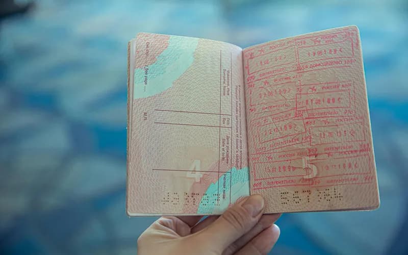 Les mains d'un voyageur tenant un document imprimé près d'un passeport sur une table en bois, lumière naturelle douce provenant d'une fenêtre, gros plan
