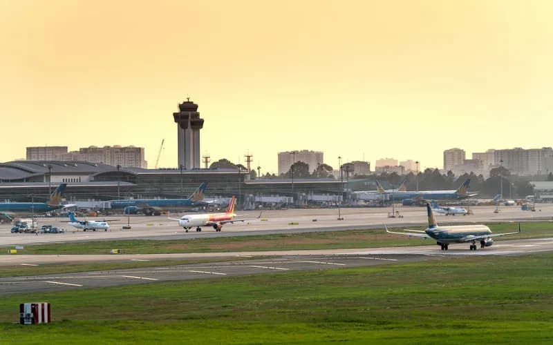 a wide exterior view of Tan Son Nhat International Airport terminal building at dusk, golden and purple sky, vehicles and tra
