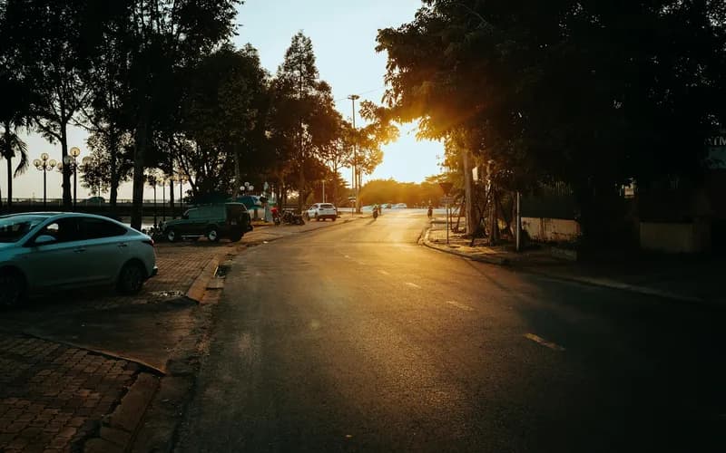 a quiet street in a Vietnamese old town at golden hour, a lone traveler viewed from behind walking between low-rise shophouse