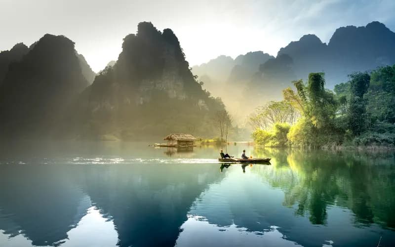 a wooden longtail boat moored on a calm river in northern Vietnam at early morning, mist rising from the water, green karst h