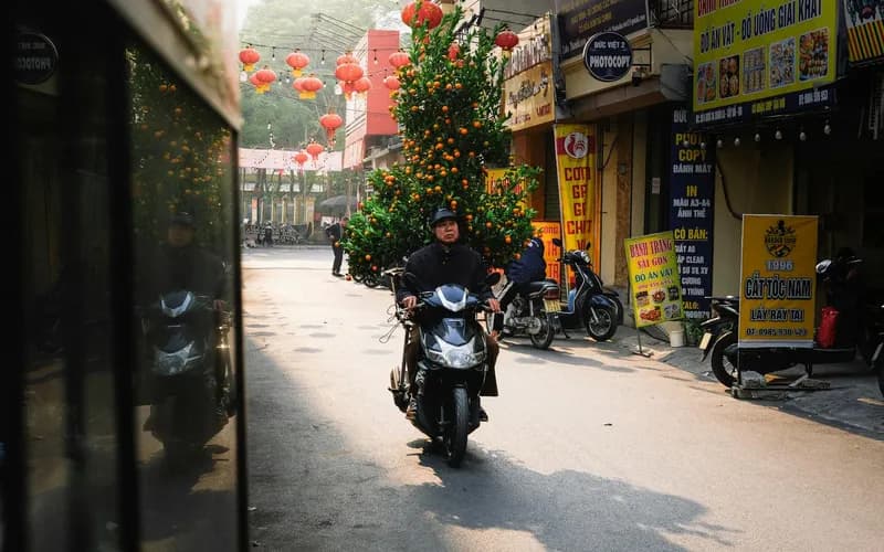 Une rue calme de Hanoi à l'aube pendant le Nouvel An lunaire, lanternes rouges tendues entre les maisons de ville, une silhouette solitaire marchant au loin