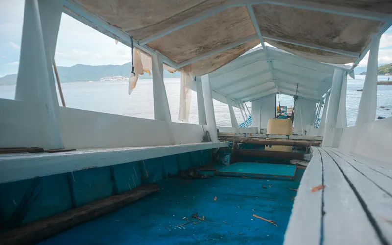 Intérieur d'une petite cabine en bois sur une baie vietnamienne, lumière chaude d'une lanterne, mobilier en rotin, un hublot donnant sur des eaux calmes