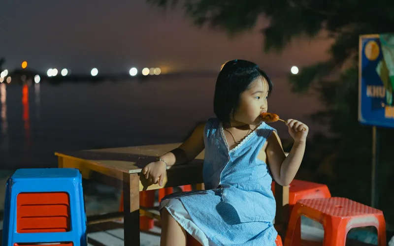 A Vietnamese family of three generations seated around a low wooden table on an open-air terrace overlooking a river at dusk,