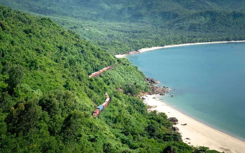 Un train de voyageurs longue distance longeant la côte vietnamienne à l'heure dorée, la mer de Chine méridionale visible au loin