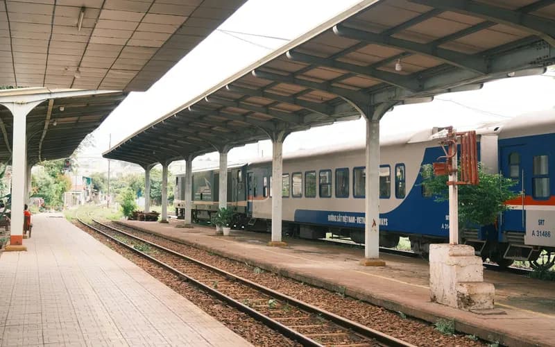 Une gare provinciale vietnamienne tranquille à l'aube, un seul quai, quelques voyageurs avec leurs bagages assis sur des bancs en bois