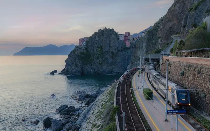A Vietnamese coastal railway line curving along a clifftop above the South China Sea at golden hour, viewed from a low angle