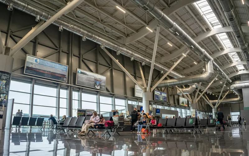 The interior of a Vietnamese domestic airport departures hall in the early morning, travelers seated with luggage, soft overh