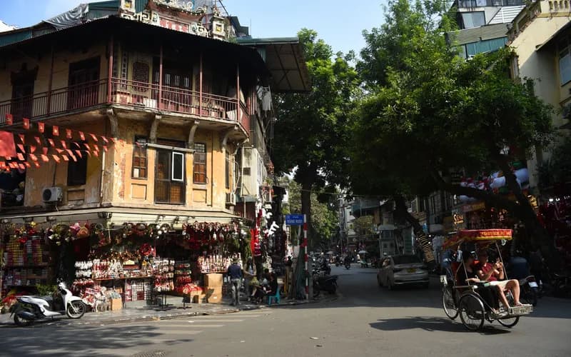 a quiet street in the old quarter of a Vietnamese city at golden hour, a traveler seated at an outdoor café table viewed from