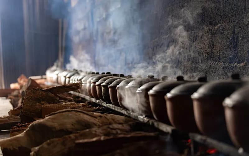 Interior of a traditional wooden bathhouse in a highland village, large clay pot over a low fire, steam rising, warm amber li