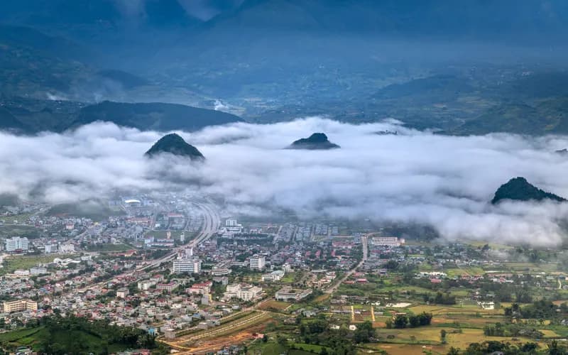 Une vallée de montagne brumeuse à l'aube dans le nord du Vietnam, des pentes boisées de pins s'élevant dans les nuages bas, un pavillon en bois solitaire visible au loin
